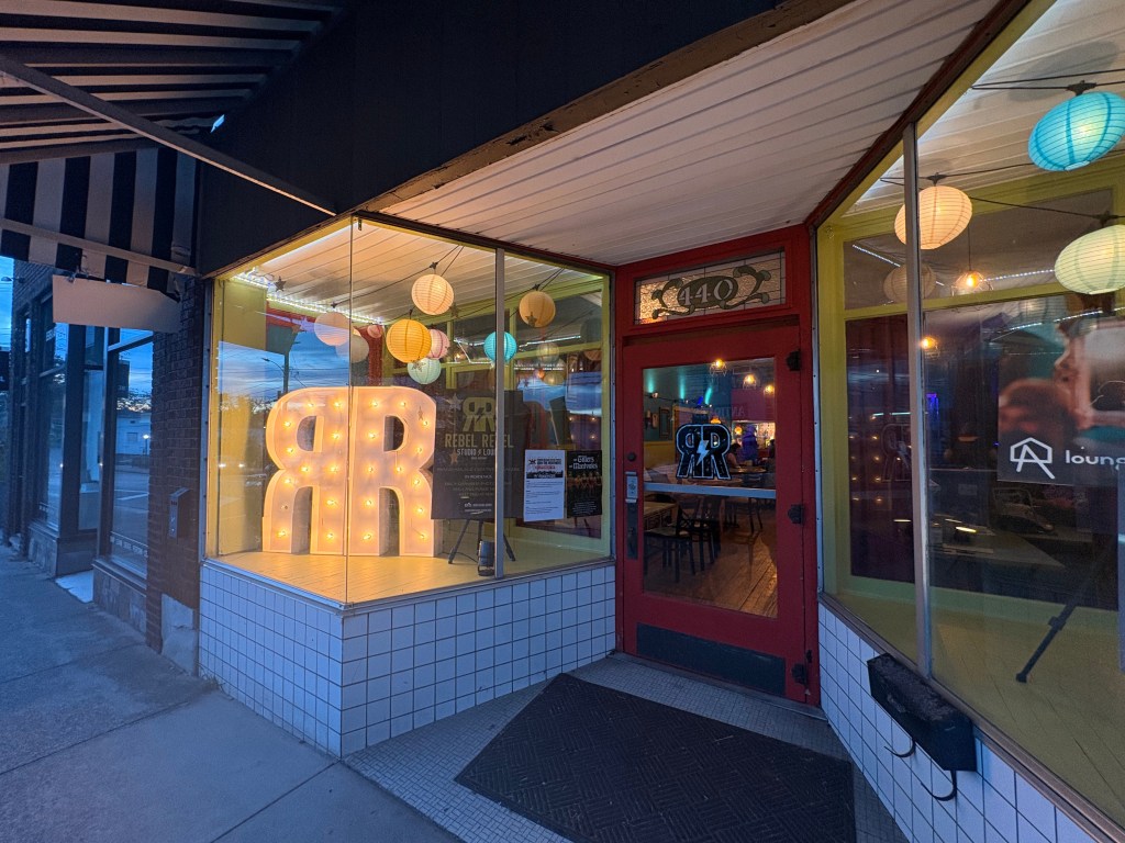 The exterior of Rebel Rebel. The window display on the left features two Rs with lightbulbs inside them making up the logo (a backwards R and a forwards R connected at their long upright lines).