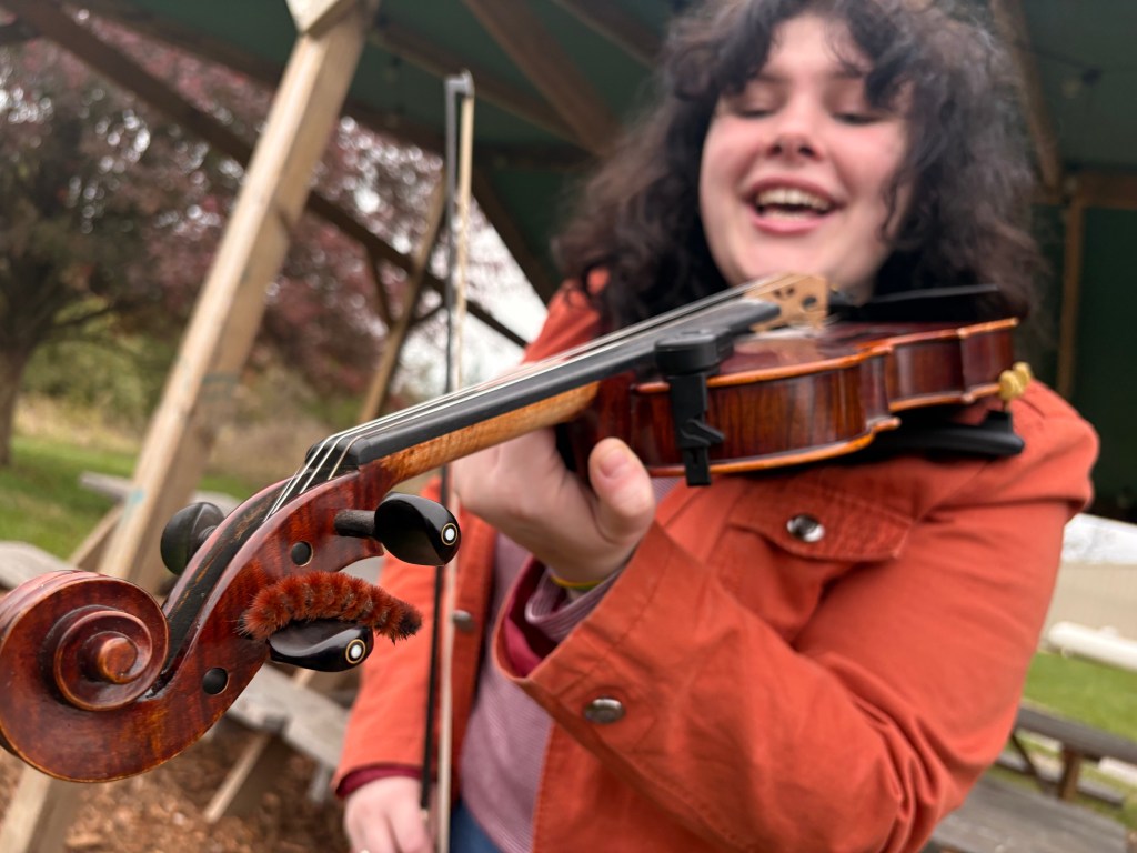 Violet laughs as a woolly worm perches on a tuning peg of her fiddle.