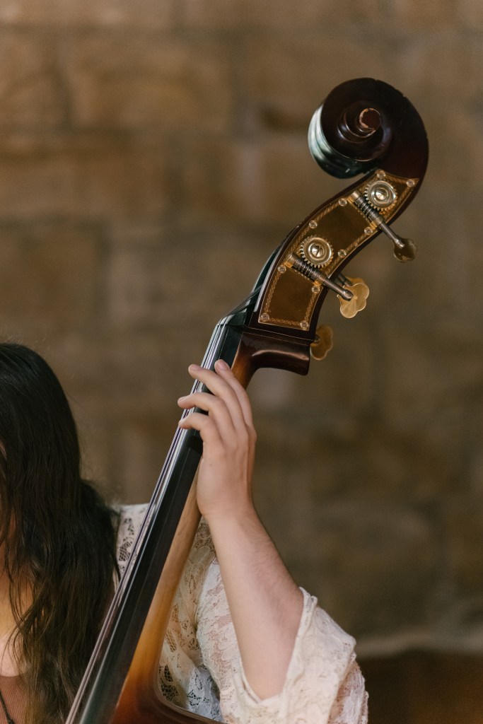 Close-up color photo of Anabel's arm and the neck of her bass. She supports the instrument lightly, her fingers curved around its neck gently.