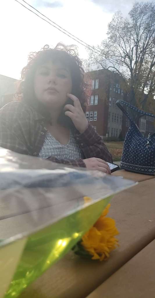 Very beautiful picture of Violet sitting at a picnic table, looking at the camera, on Morehead State's campus. A yellow flower is in the foreground.